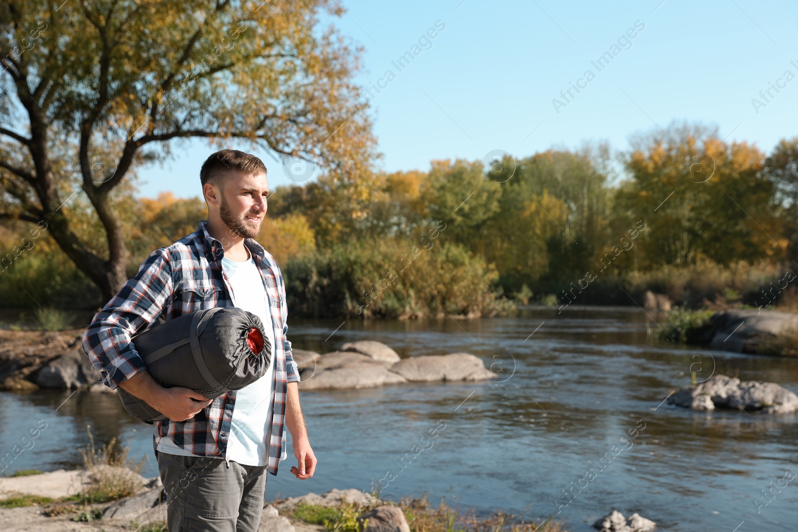Photo of Male camper with sleeping bag near pond. Space for text