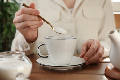 Photo of Woman adding sugar into aromatic tea at wooden table indoors, closeup