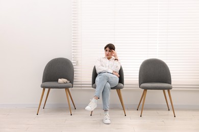 Photo of Woman sitting on chair and waiting for appointment indoors