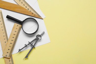 Photo of Different rulers, magnifying glass and compass on yellow background, flat lay. Space for text