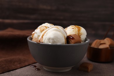 Scoops of ice cream with caramel sauce and candies on textured table, closeup