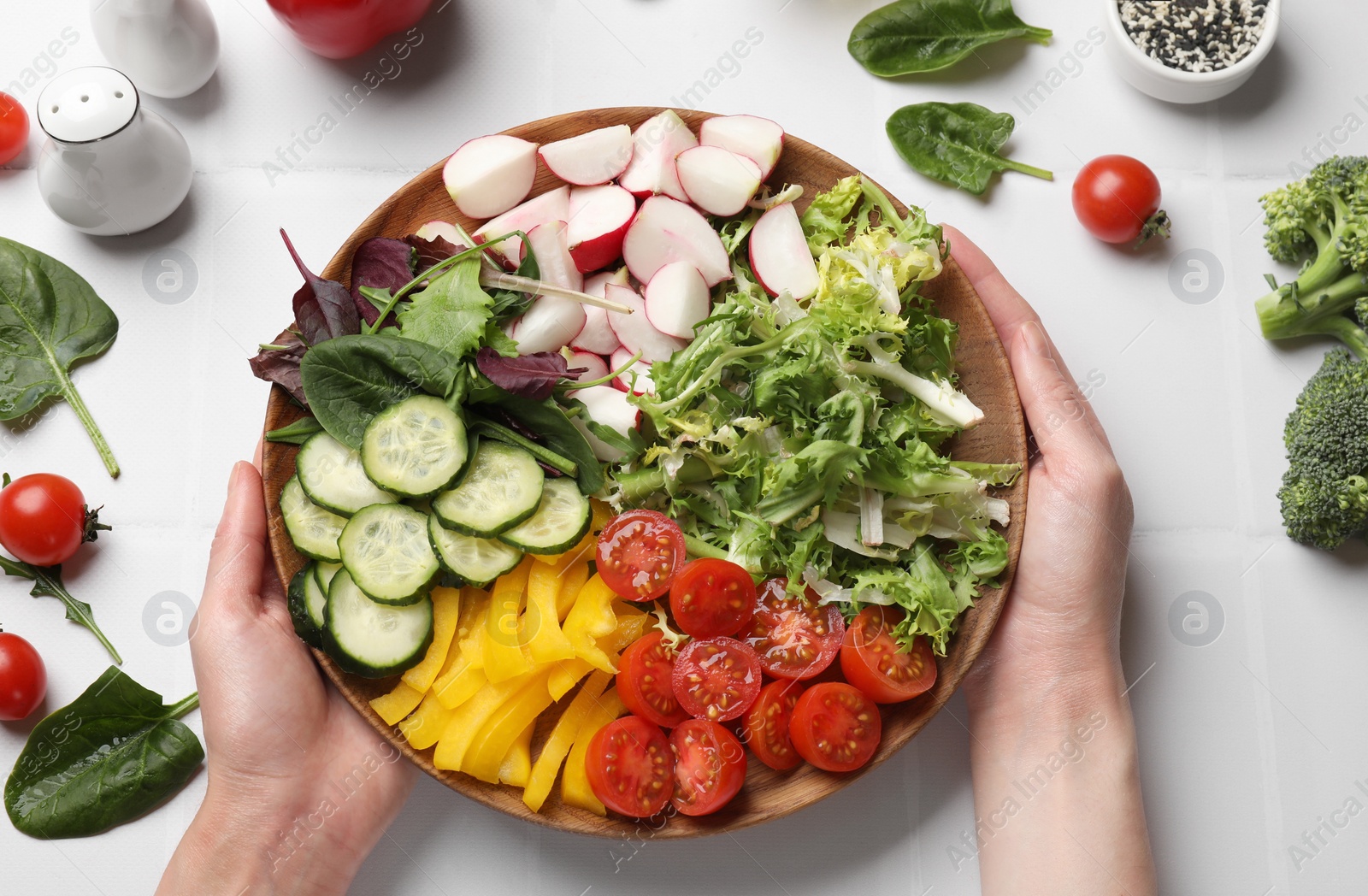 Photo of Vegetarian diet. Woman with plate of tasty vegetables at white tiled table, top view