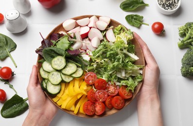 Photo of Vegetarian diet. Woman with plate of tasty vegetables at white tiled table, top view