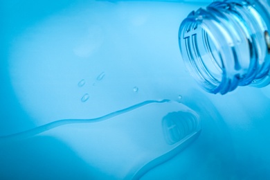 Photo of Drops of spilled water and plastic bottle on light blue background, closeup