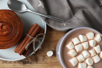 Photo of Composition with delicious hot cocoa drink and bun on wooden background, flat lay
