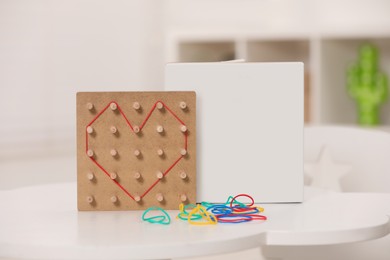 Photo of Wooden geoboard with rubber bands on white table indoors. Educational toy for motor skills development