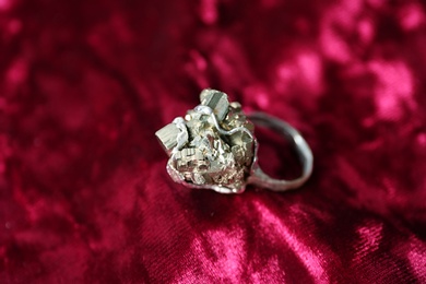 Photo of Beautiful silver ring with pyrite gemstones on burgundy fabric, closeup