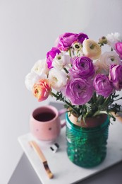 Image of Bouquet of beautiful ranunculuses and tea on table near light grey wall
