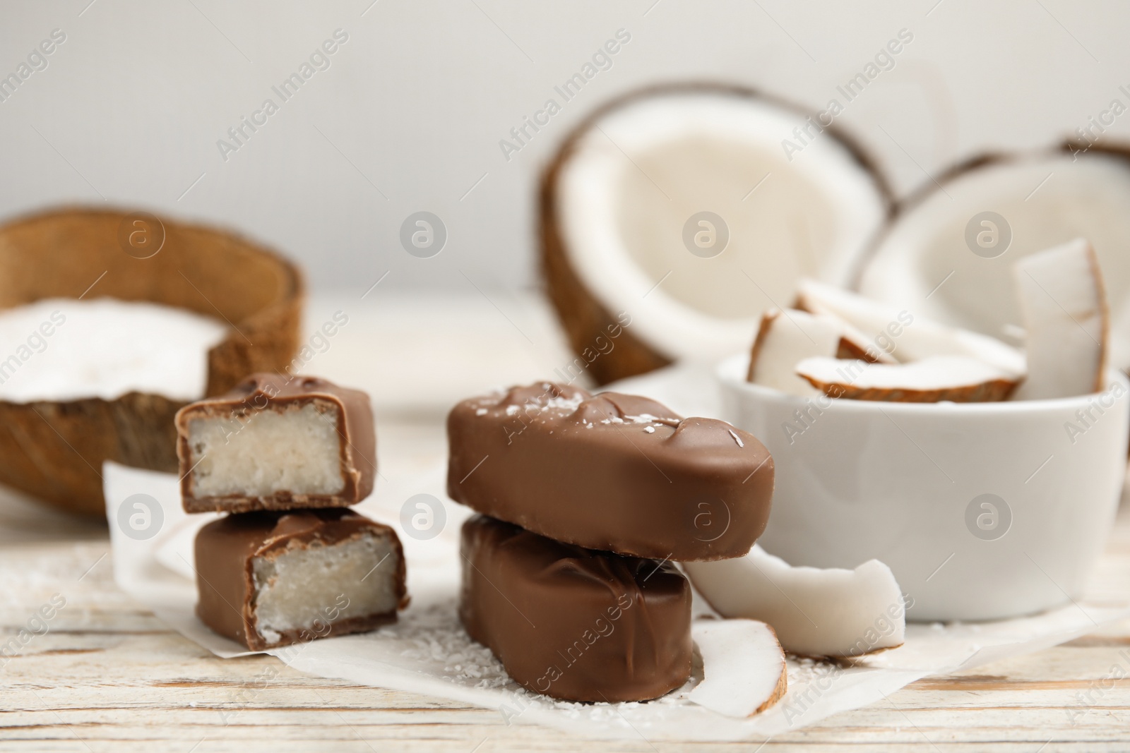 Photo of Delicious milk chocolate candy bars with coconut filling on white wooden table, closeup. Space for text