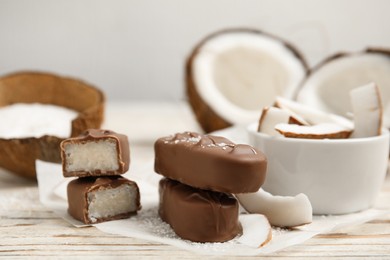 Delicious milk chocolate candy bars with coconut filling on white wooden table, closeup. Space for text