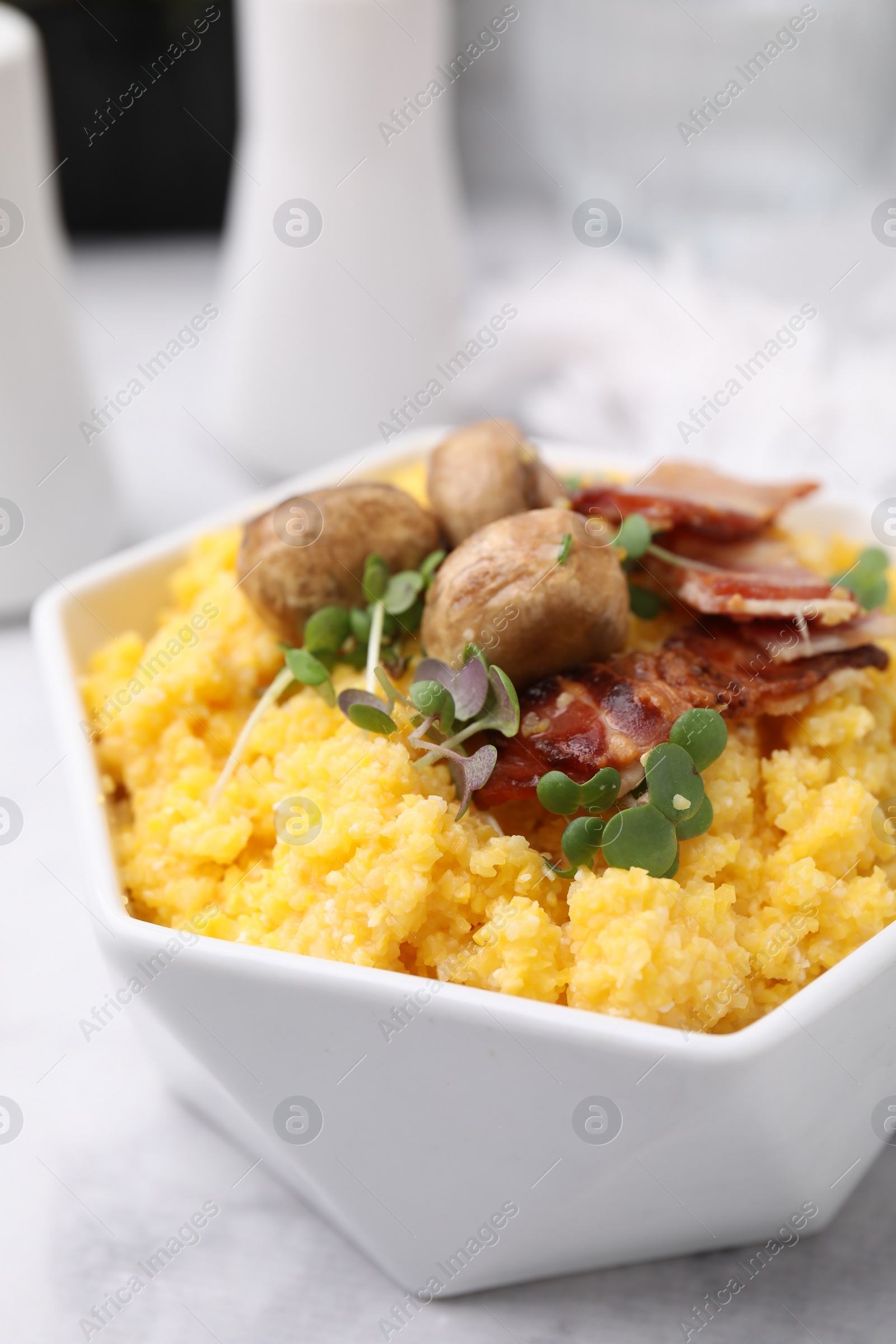 Photo of Cooked cornmeal with bacon, mushrooms and microgreens in bowl on white marble table, closeup