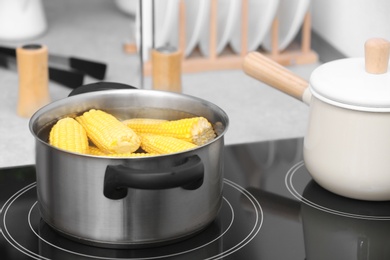 Photo of Stewpot with water and corn cobs on stove in kitchen