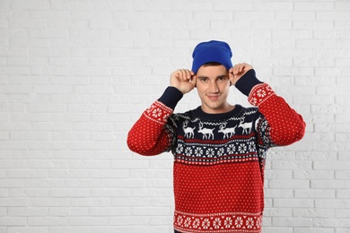 Photo of Portrait of young man in Christmas sweater and hat near white brick wall. Space for text