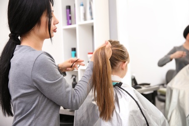 Photo of Professional female hairdresser working with little girl in salon