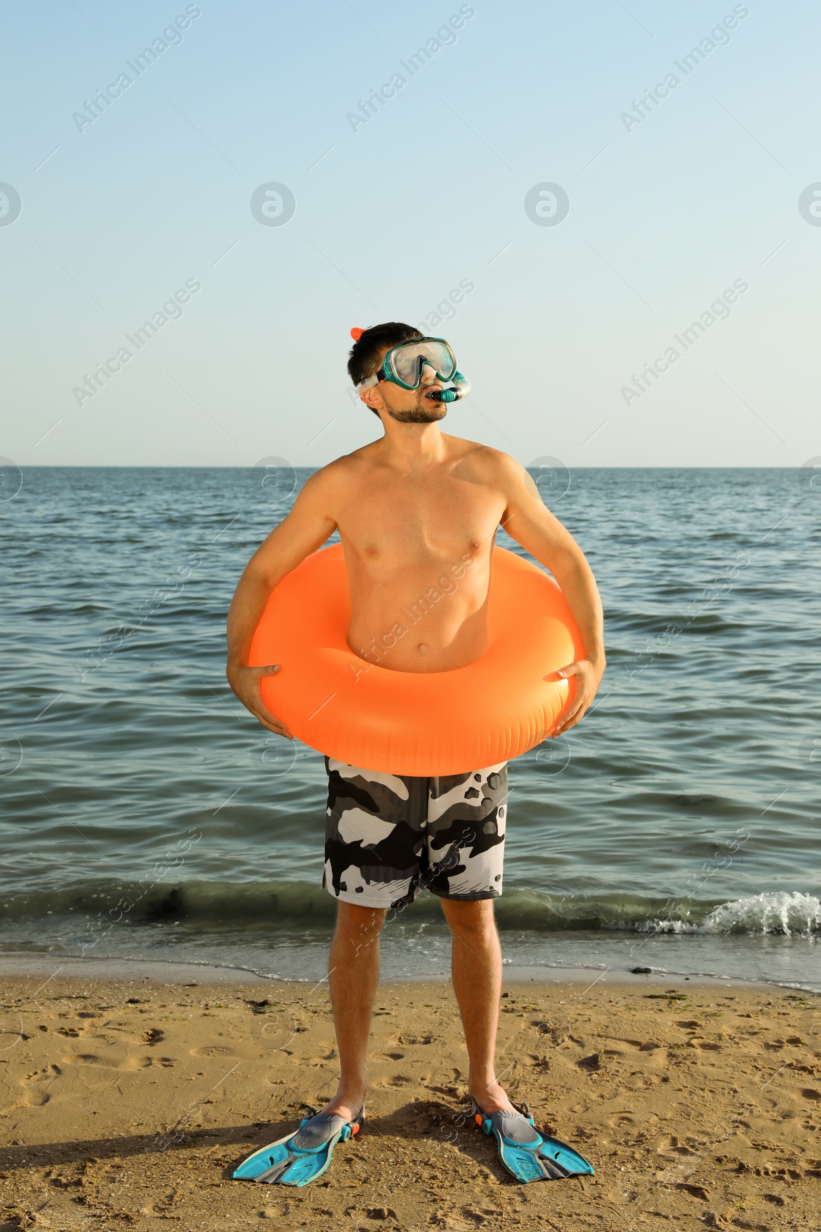 Photo of Man with flippers, inflatable ring and goggles on sea beach