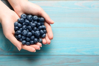 Photo of Woman with heap of tasty blueberries on light blue wooden background, top view. Space for text