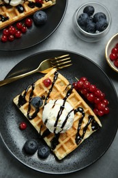 Photo of Delicious Belgian waffles with ice cream, berries and chocolate sauce on grey table, flat lay