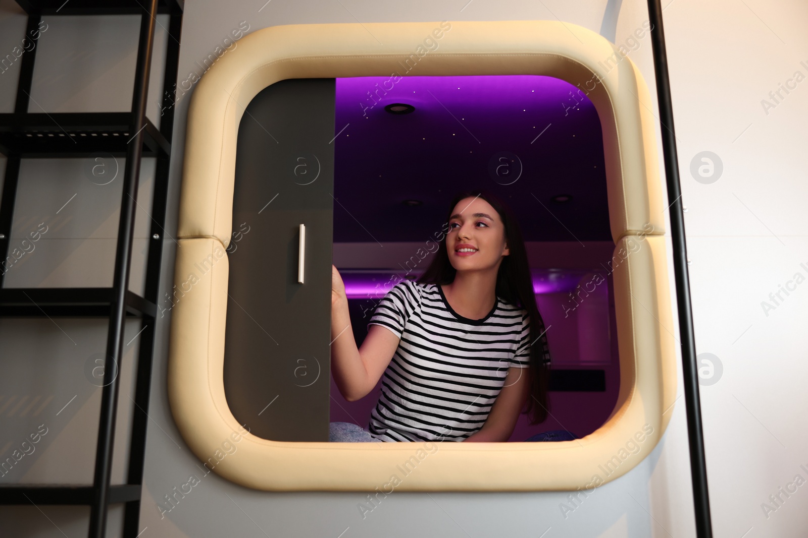 Photo of Happy young woman closing door of capsule in pod hostel