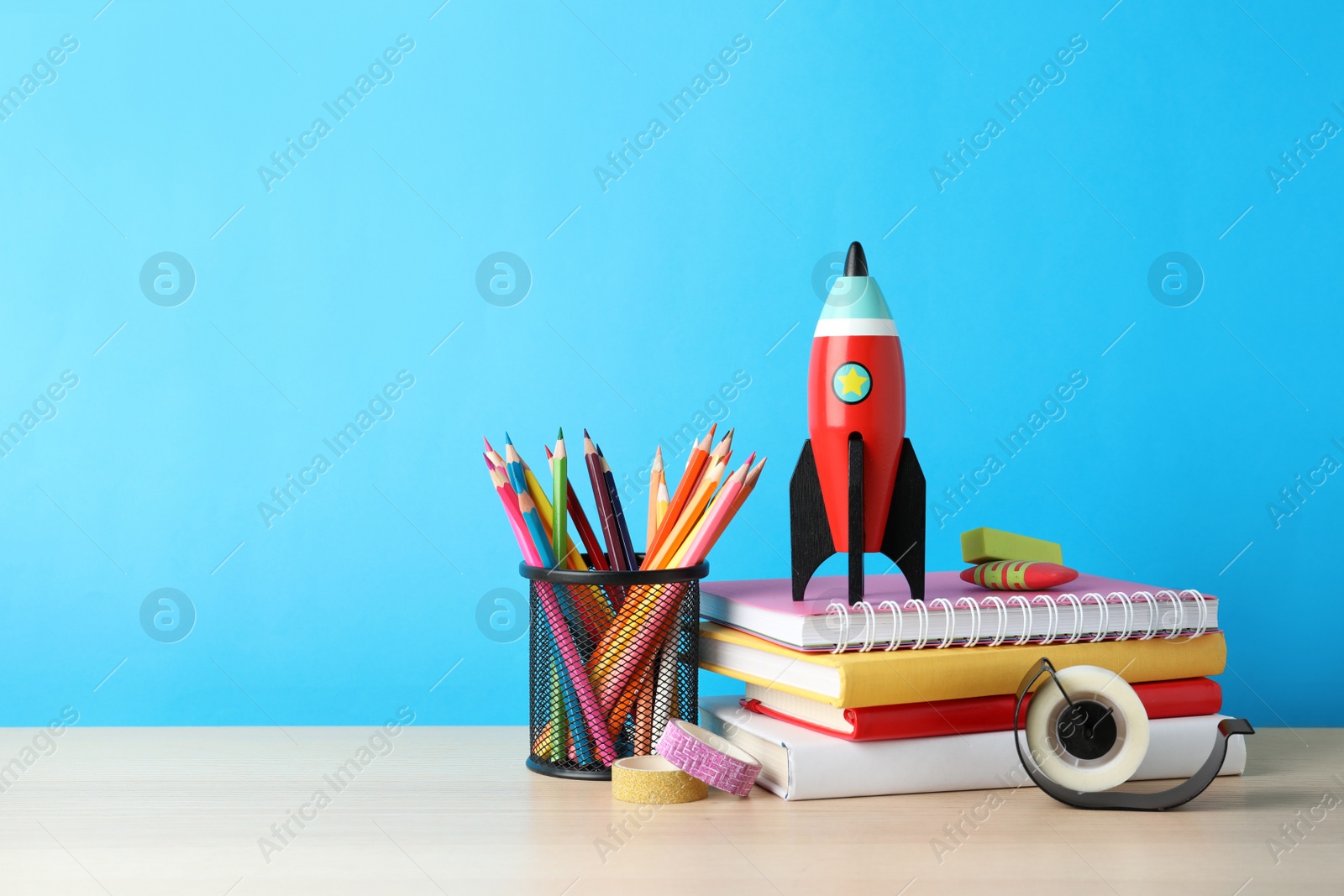 Photo of School stationery and rocket on wooden table against light blue background