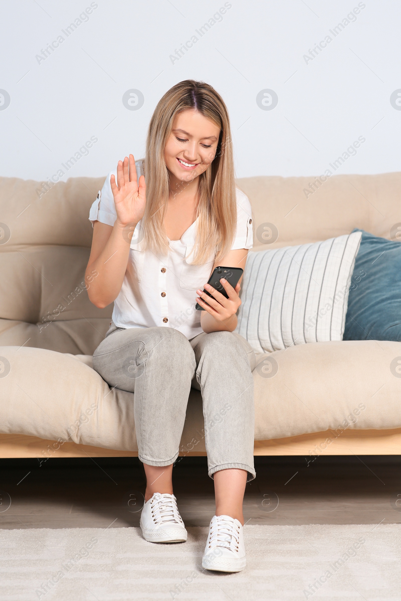 Photo of Woman with smartphone having video chat on sofa at home