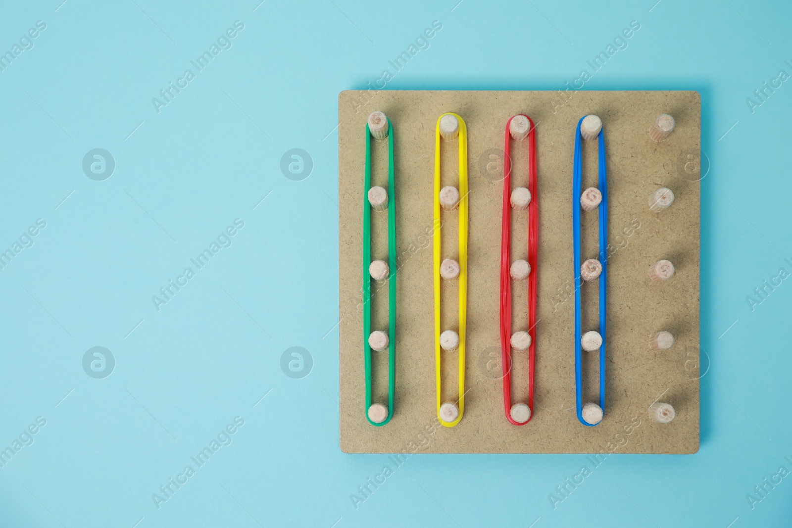 Photo of Wooden geoboard with rubber bands on light blue background, top view and space for text. Educational toy for motor skills development