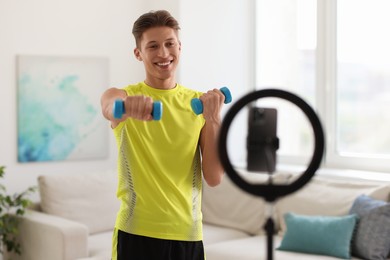 Smiling sports blogger working out with dumbbells while streaming online fitness lesson at home