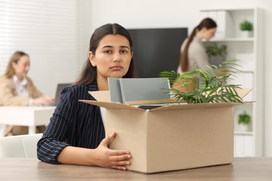 Unemployment problem. Frustrated woman with box of personal belongings at table in office