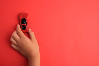 Photo of Child playing with toy car on red background, top view. Space for text