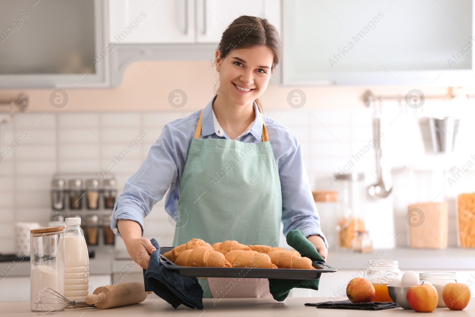 Photo of Woman holding baking tray with delicious croissants in kitchen