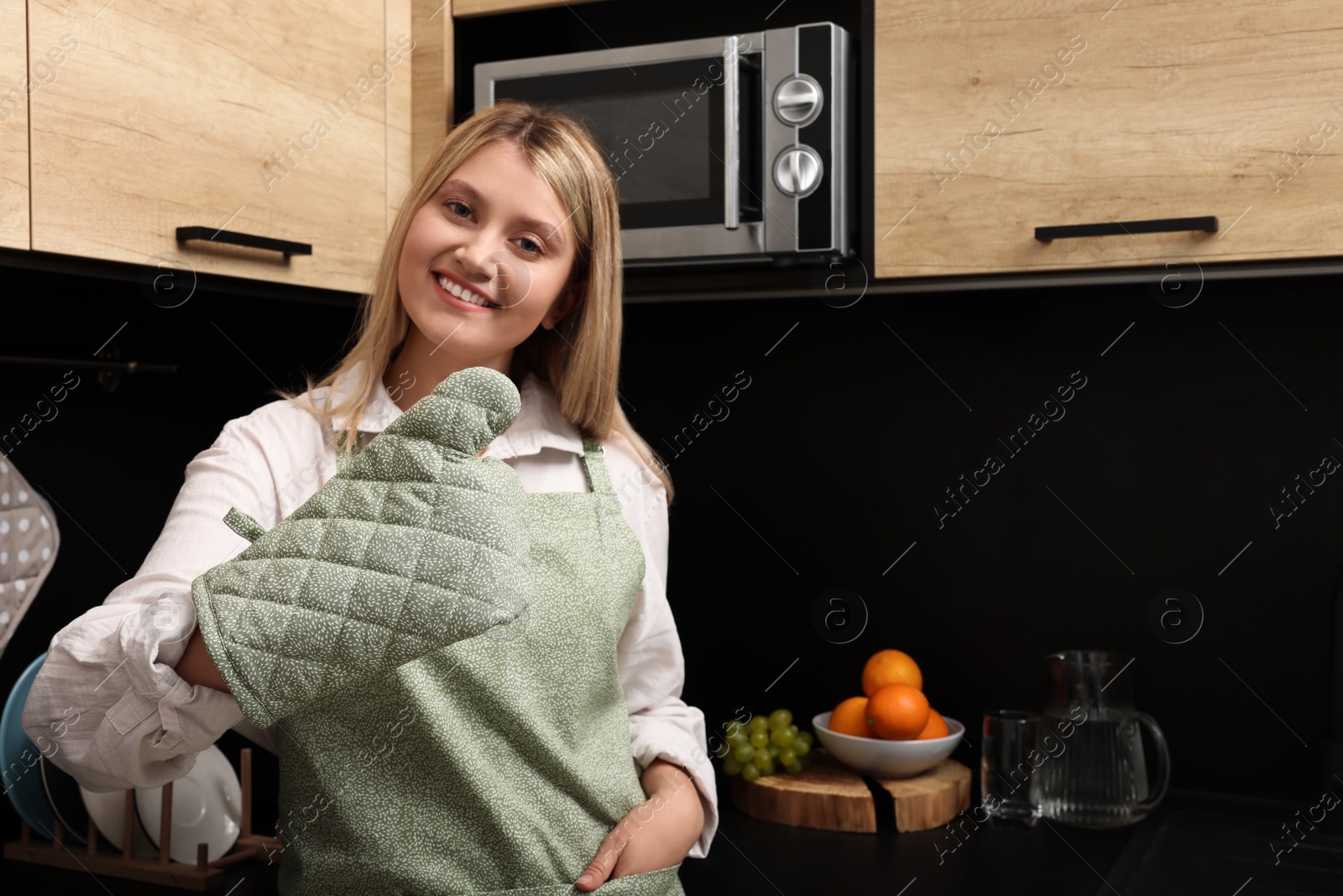 Photo of Beautiful young woman in clean apron and oven glove at kitchen