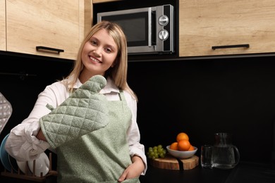 Beautiful young woman in clean apron and oven glove at kitchen