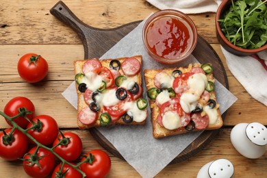 Photo of Tasty pizza toasts, sauce, arugula and tomatoes on wooden table, flat lay