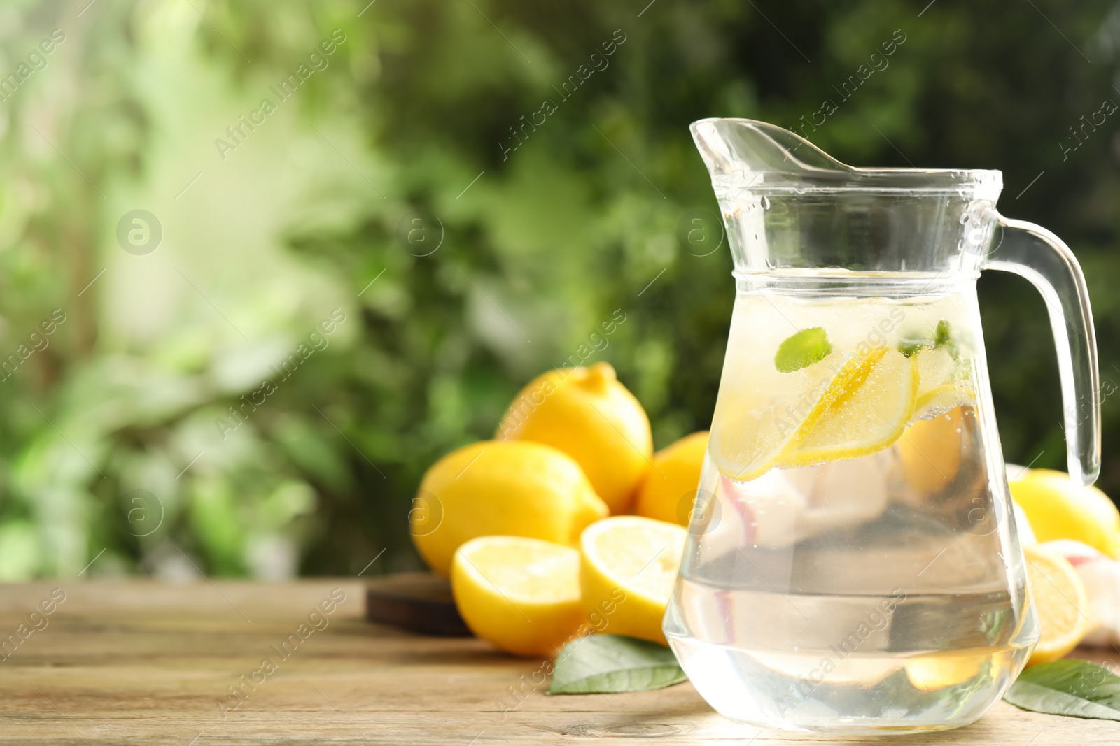 Photo of Glass jug of cold lemonade on wooden table. Space for text