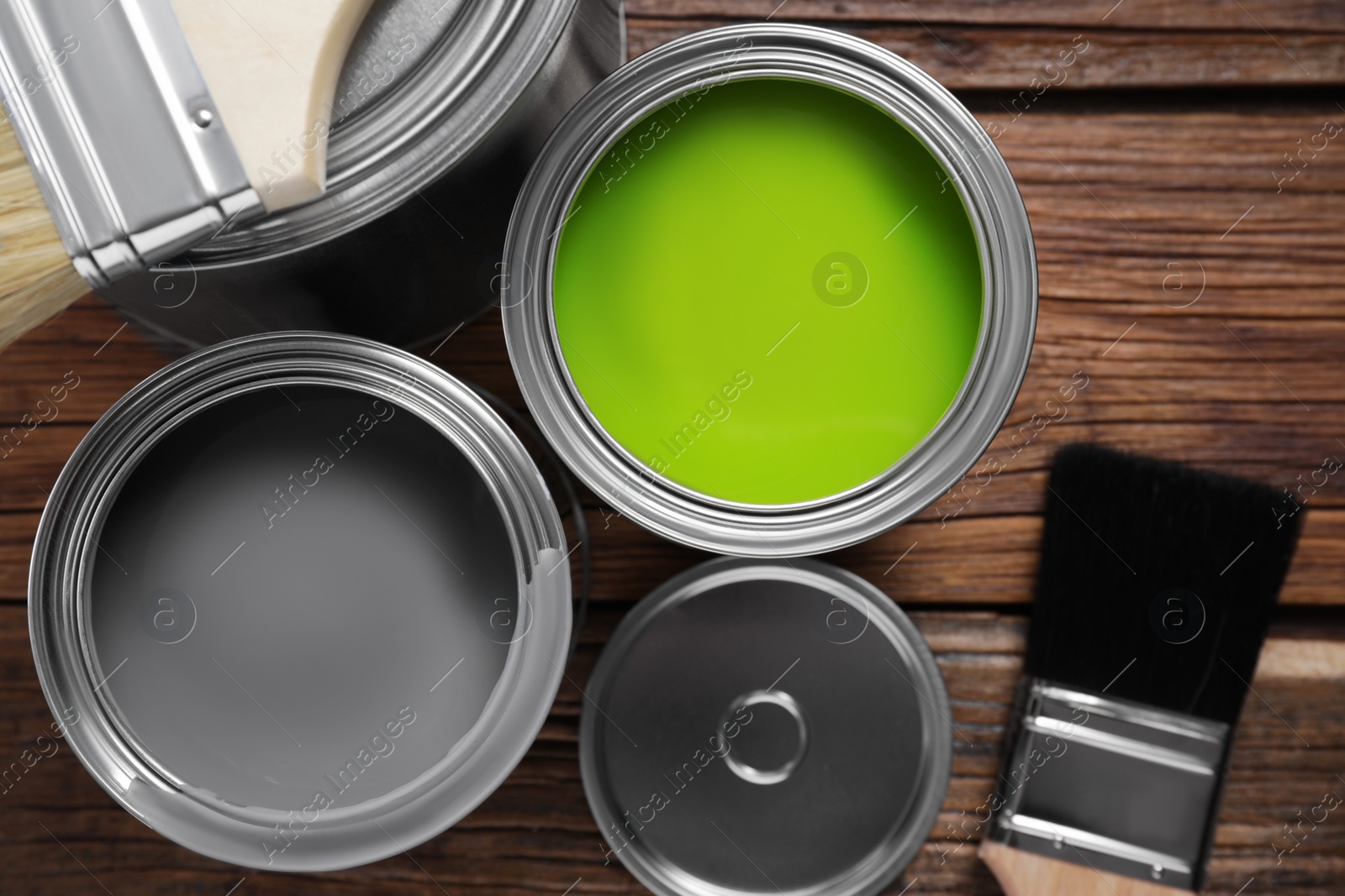 Photo of Cans of paints and brushes on wooden table, flat lay