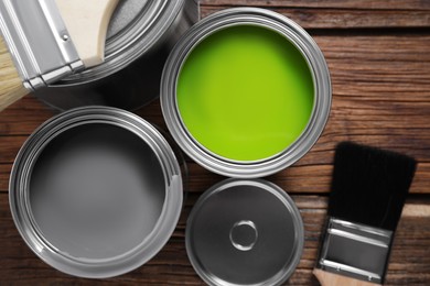 Photo of Cans of paints and brushes on wooden table, flat lay