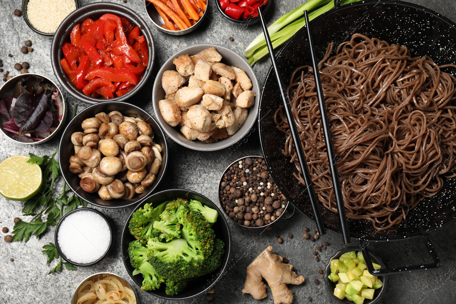 Photo of Wok with noodles, chicken and other products on grey table, flat lay