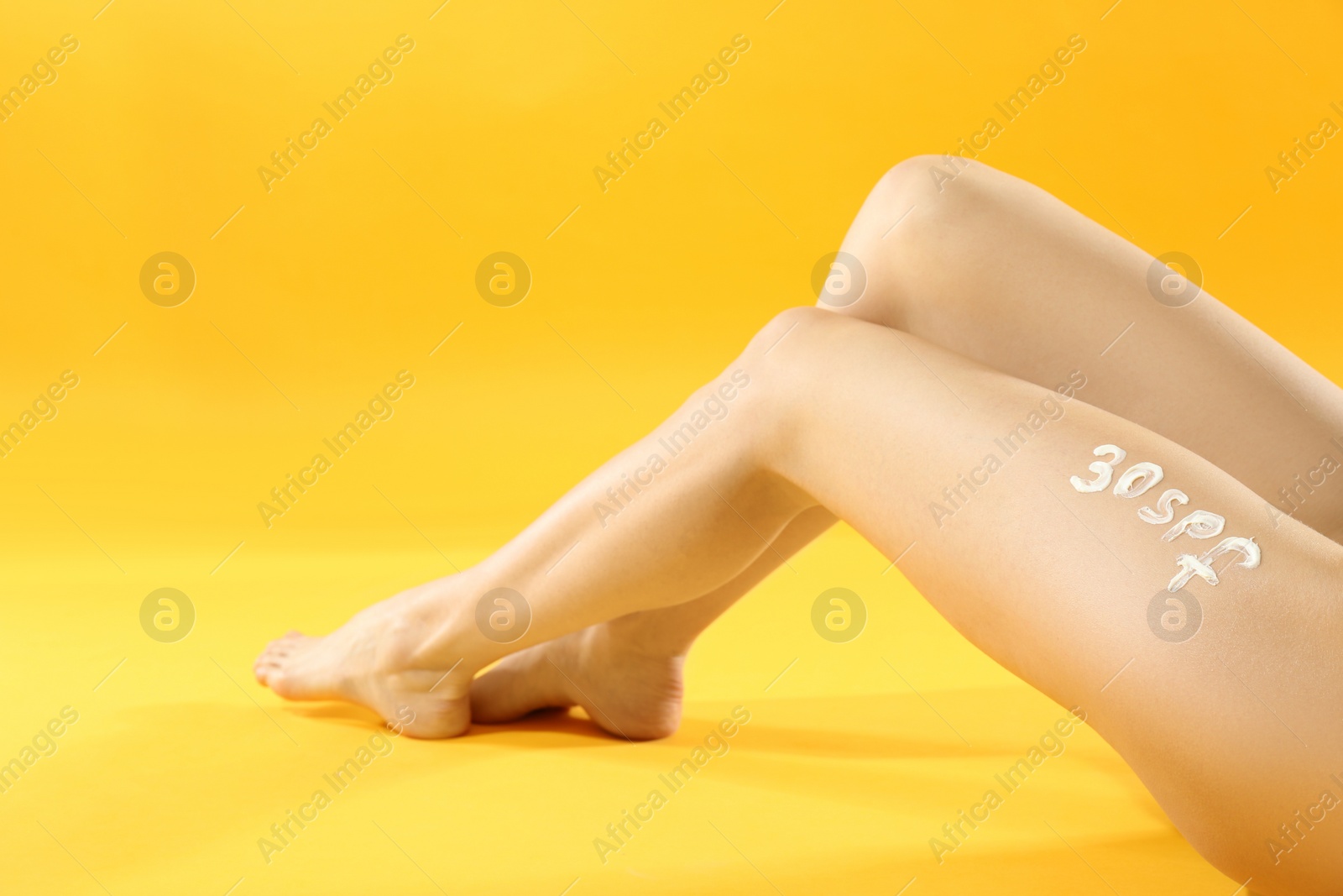 Photo of Text 30 SPF written with sun protection cream on woman's leg against yellow background, closeup