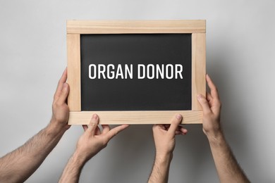 Men holding chalkboard with text ORGAN DONOR  on light background