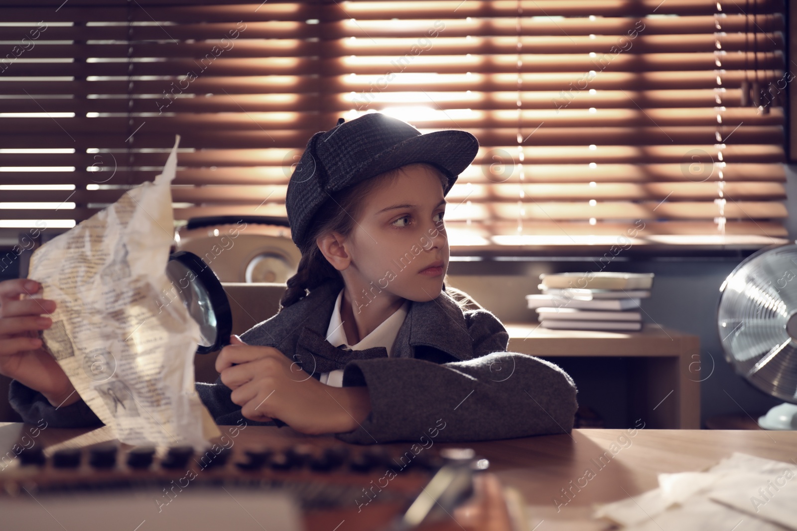 Photo of Cute little detective with document and magnifying glass at table in office