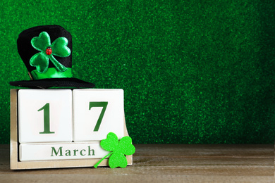 Black leprechaun hat, clover leaf and wooden block calendar on table, space for text. St. Patrick's Day celebration