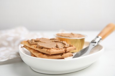 Photo of Crispy crackers with delicious meat pate and knife on white table, closeup