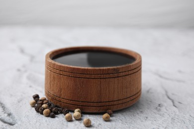 Photo of Wooden bowl with balsamic vinegar and peppercorns on white textured table, closeup