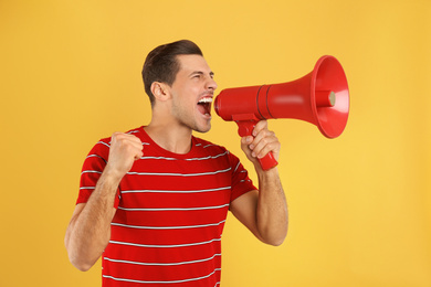 Handsome man with megaphone on yellow background