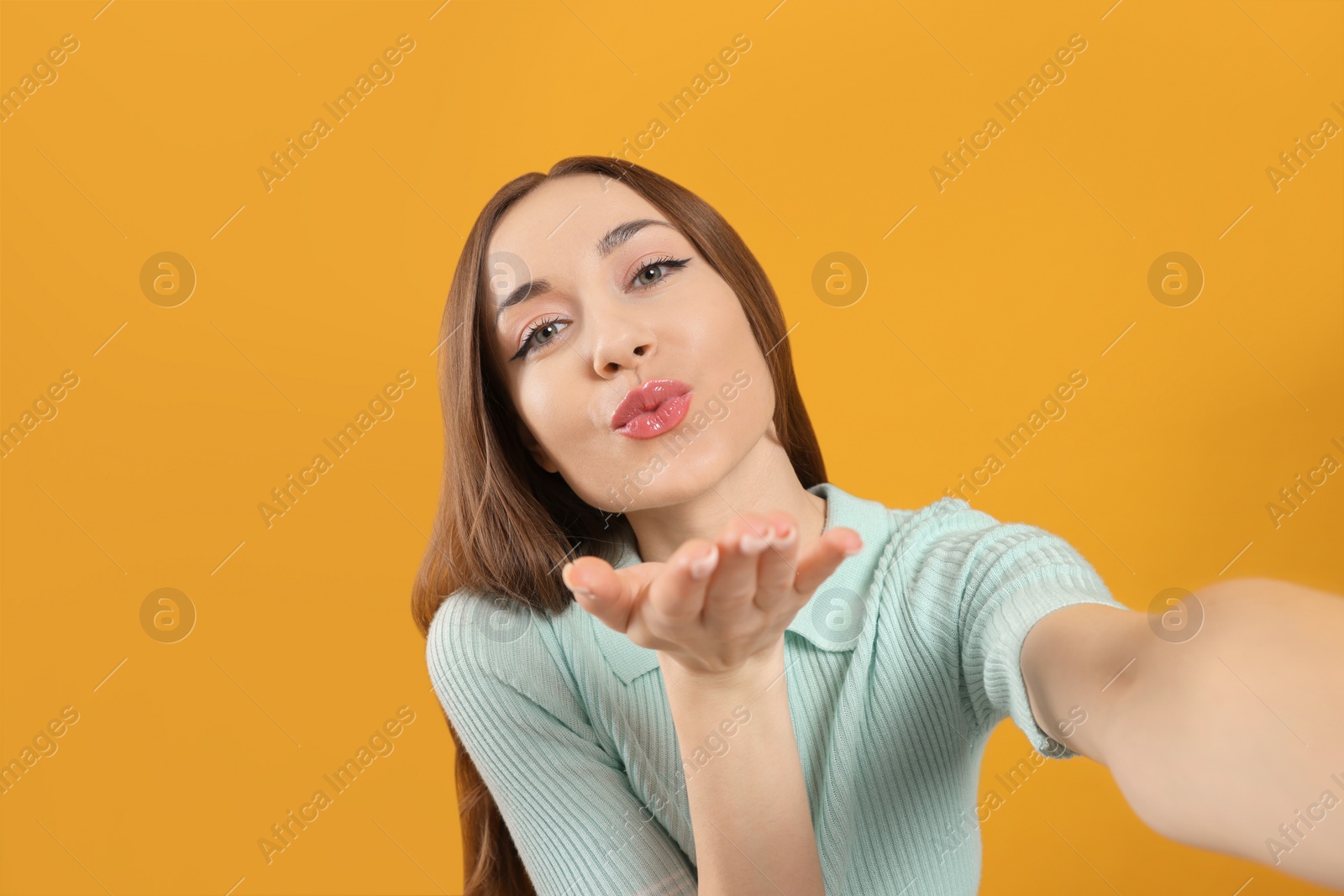 Photo of Beautiful young woman blowing kiss while taking selfie on yellow background