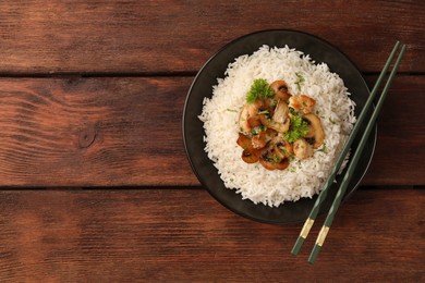 Delicious rice with mushrooms, parsley and chopsticks on wooden table, top view. Space for text