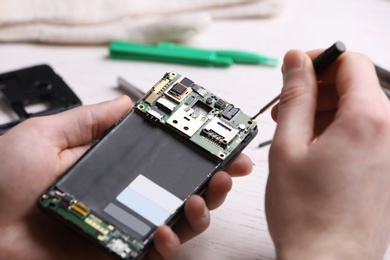 Technician fixing mobile phone at table, closeup. Device repair service