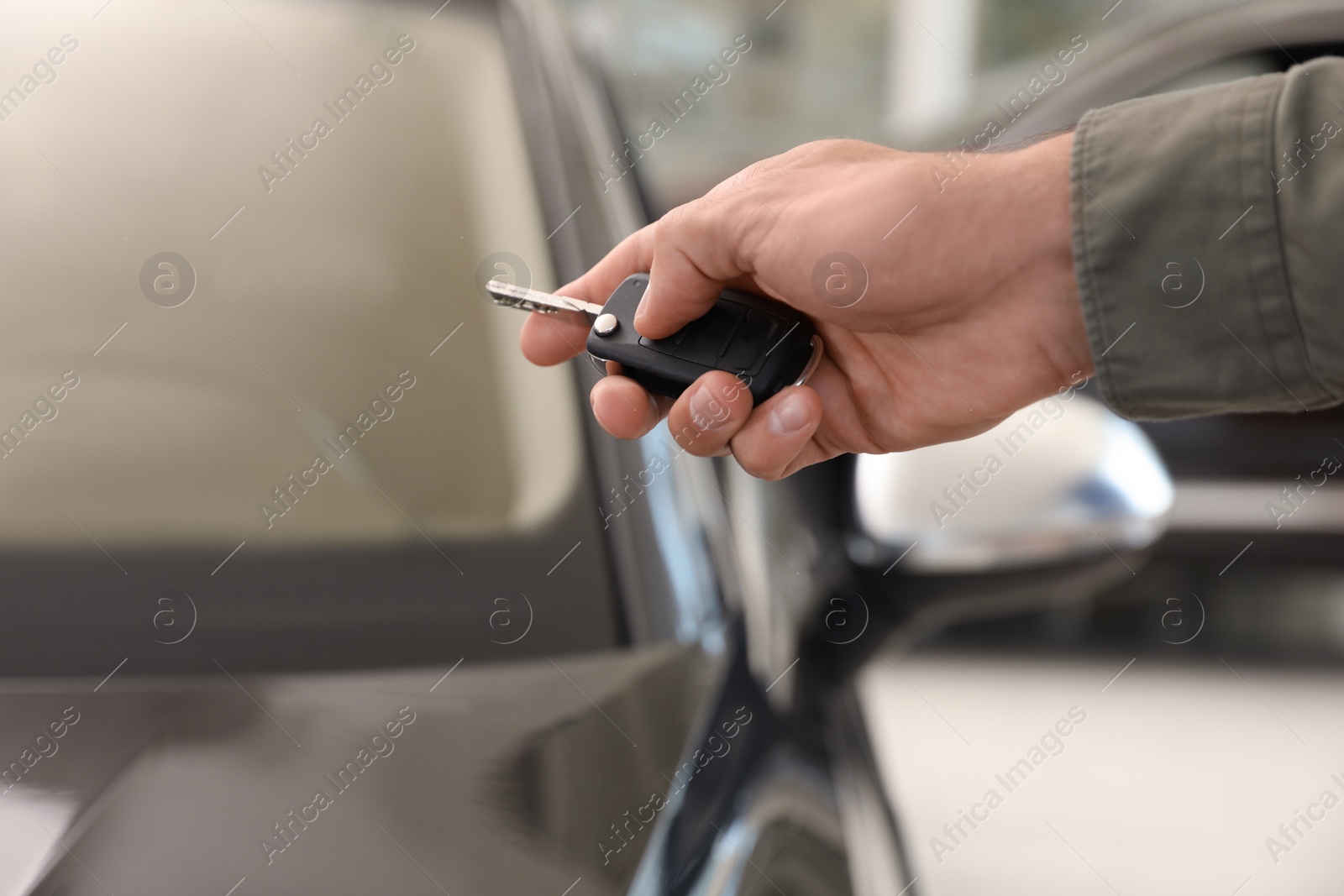 Photo of Young man checking alarm system with car key indoors, closeup