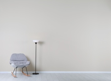 Photo of Rocking chair and lamp near color wall with space for text. Interior element