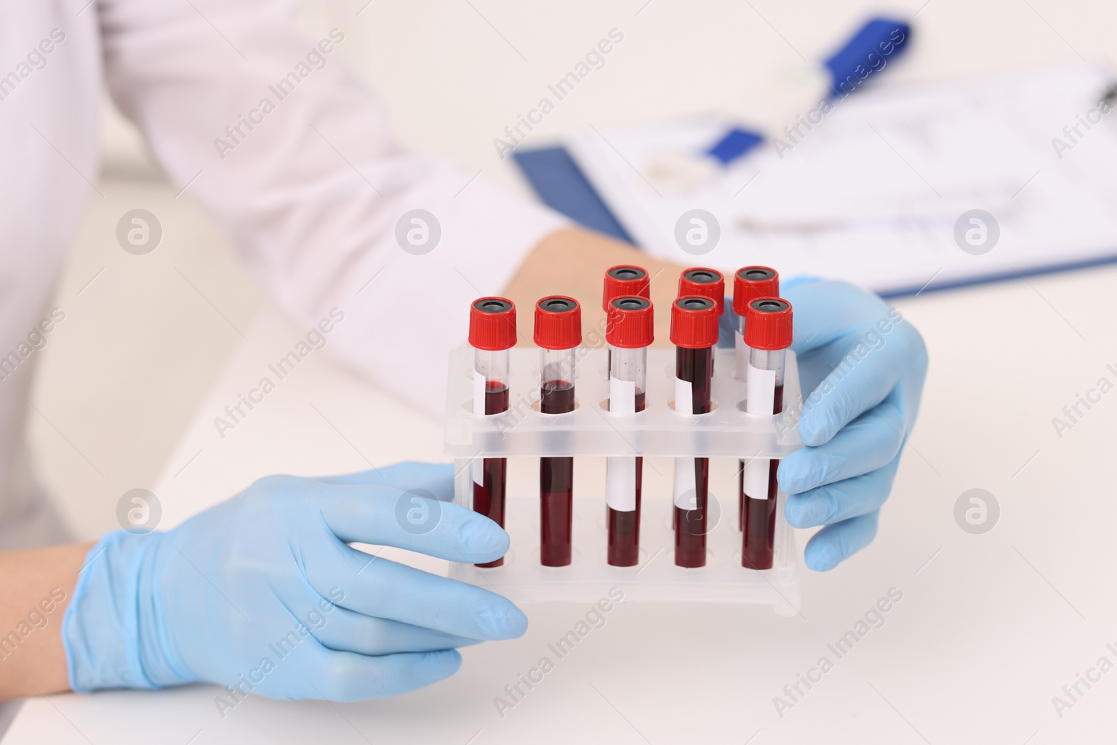 Photo of Doctor with samples of blood in test tubes at white table, closeup