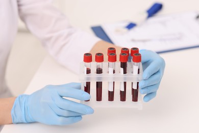 Photo of Doctor with samples of blood in test tubes at white table, closeup